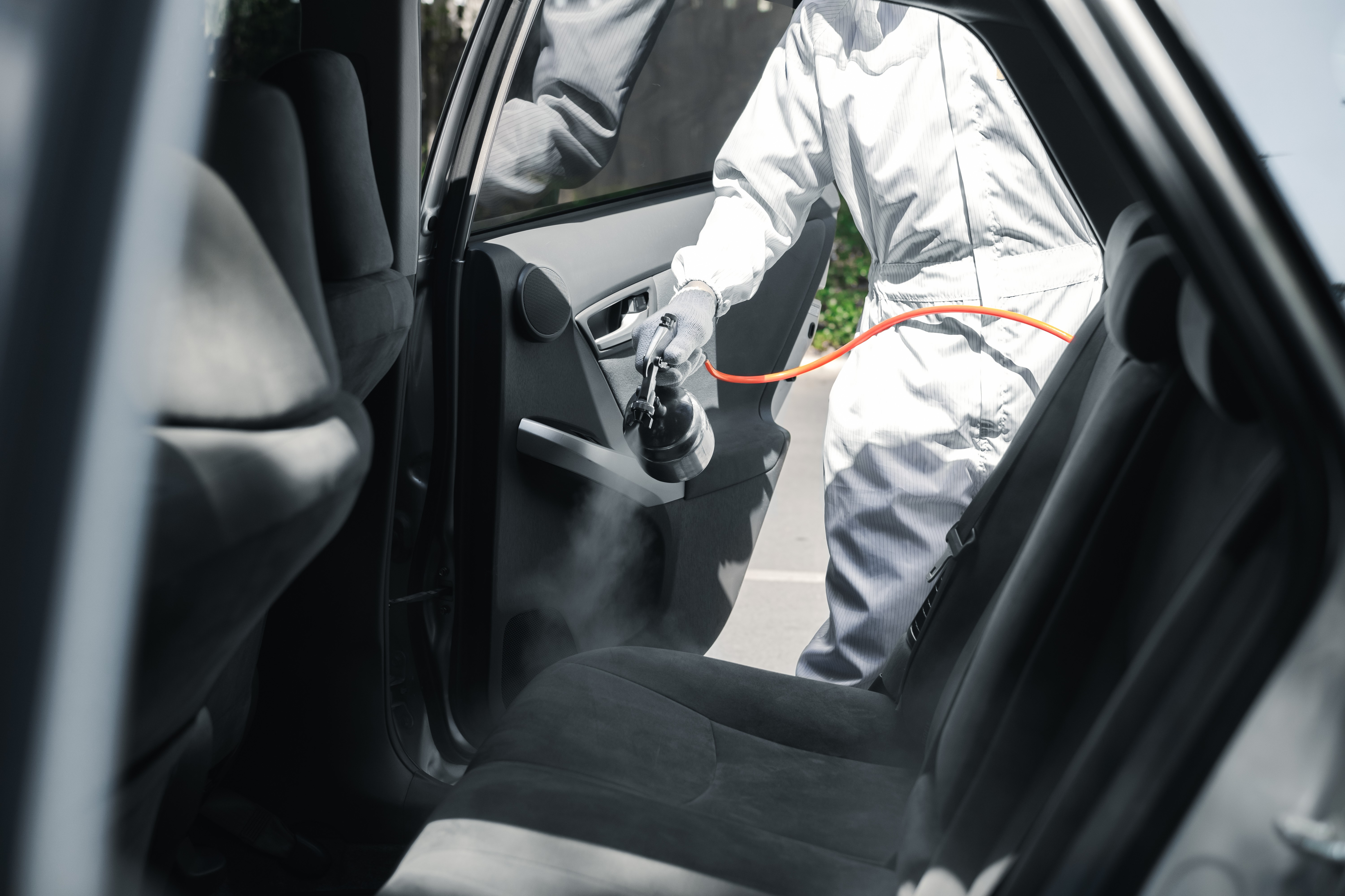 Car Wash Employee Wearing PPE and Spraying Disinfectant in Interior Car